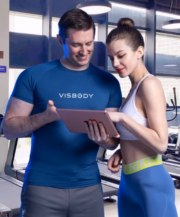 Trainer im Visbody-Shirt bespricht mit einer Kundin die Messergebnisse auf dem Tablet